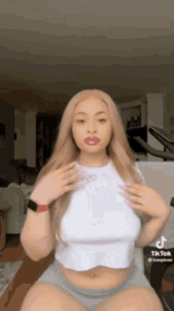 a woman in a white crop top and grey shorts is sitting on a chair in a living room .