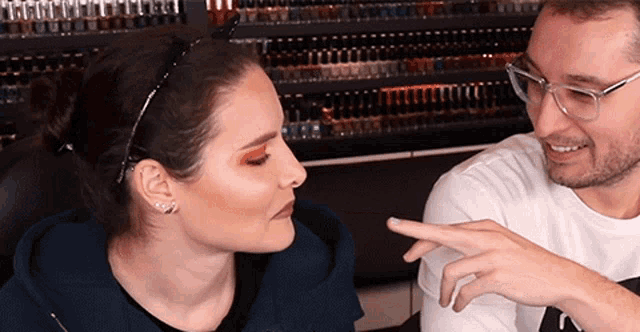 a man pointing at a woman 's finger in front of a display of nail polish