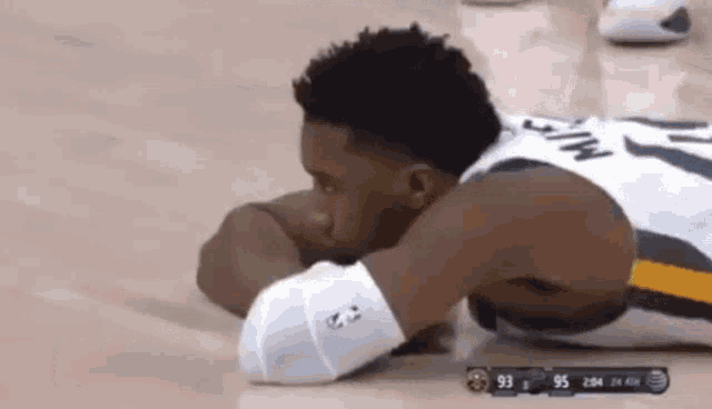 a basketball player is laying on the floor with his head on his knee .