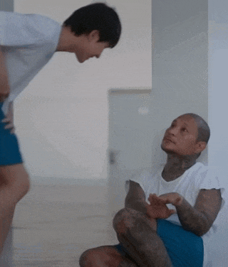 two men are talking to each other in a room . one of the men is sitting on the floor and the other is standing .