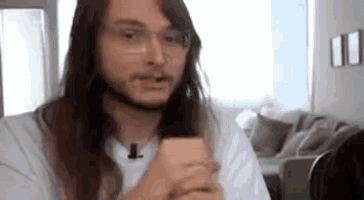 a man with long hair and glasses is looking at a cell phone .