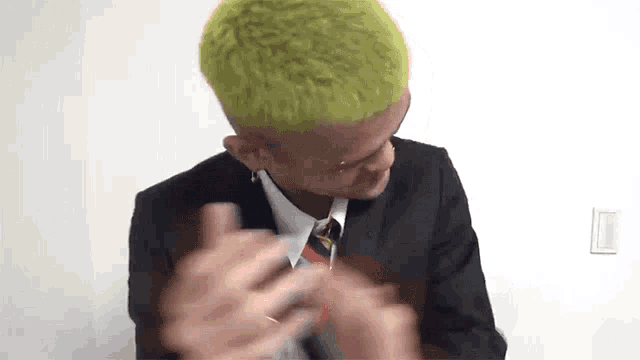 a man with green hair is wearing a suit and tie and is making a funny face .