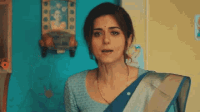 a woman in a blue blouse and a blue and silver saree is standing in front of a blue wall .