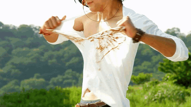 a man in a white shirt is taking off his shirt while standing in a field