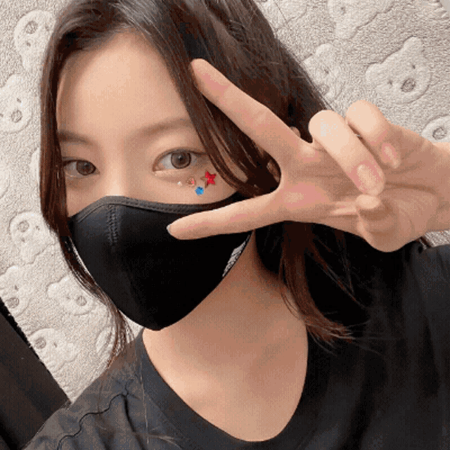 a woman wearing a black face mask is giving the peace sign