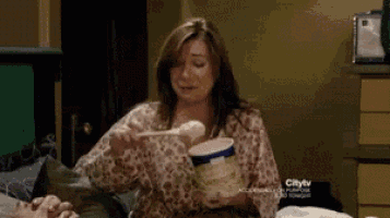 a woman is sitting on a bed with a container of ice cream in her hand