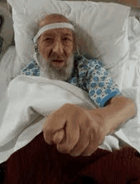 an elderly man with a beard is laying in a hospital bed with a headband on .