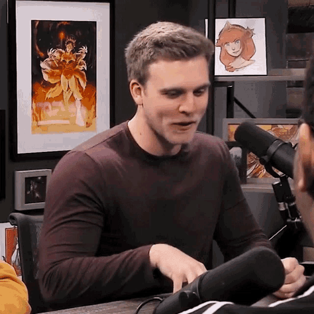 a man sitting in front of a microphone with a framed picture of a woman in the background