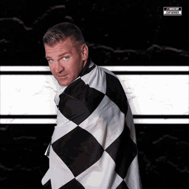 a man is wrapped in a black and white checkered flag with a nascar logo on the bottom right