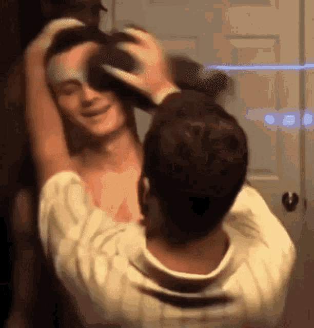 a man is holding another man 's head while they are standing next to each other in front of a mirror .