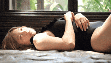 a woman in a black swimsuit is laying on the floor near a window