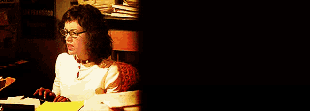 a woman wearing glasses is sitting at a desk with papers