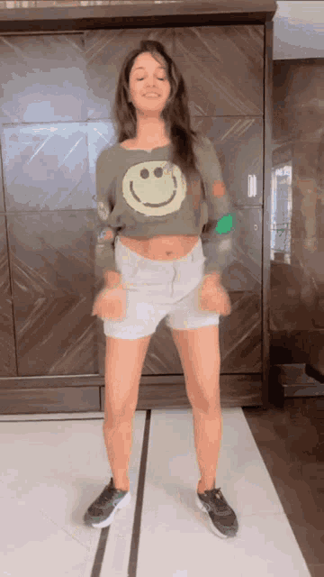 a woman in a crop top with a smiley face on it is dancing