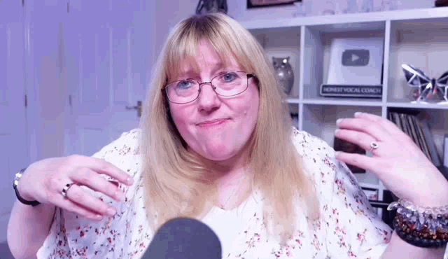 a woman wearing glasses and a ring is sitting in front of a microphone in a room .
