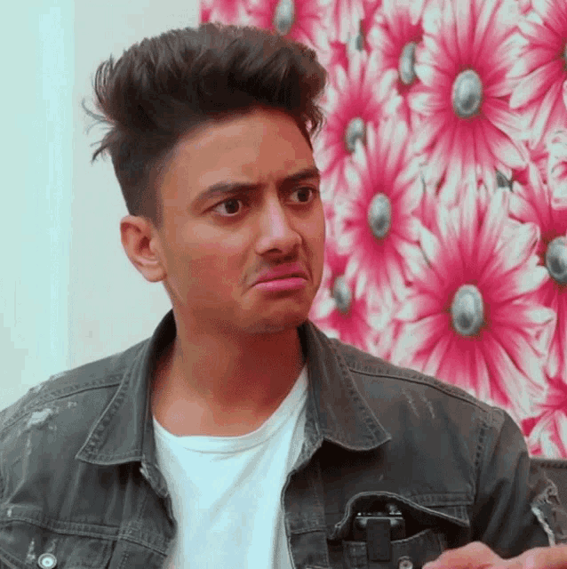 a young man making a funny face in front of a pink and white flower wallpaper