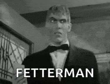 a man in a tuxedo and bow tie is standing in front of a window and says fetterman .