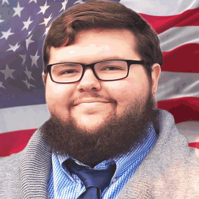 a man with glasses and a beard is smiling in front of a flag