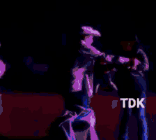 a man in a white shirt is dancing in the dark with tdk written on the bottom right