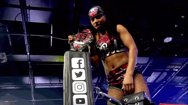 a woman in a wrestling ring holds a championship belt and stands next to a facebook logo