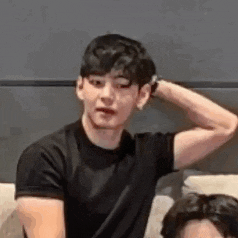 a young man in a black shirt is sitting on a couch with his hand behind his head .
