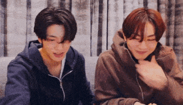 two young men are sitting next to each other on a couch laughing .