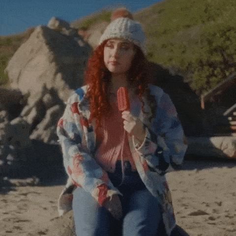 a woman with red hair is holding a popsicle in her hand
