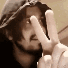 a man with a beard and a hat is making a peace sign with his hands .