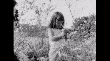 a black and white photo of a little girl picking flowers in a field .