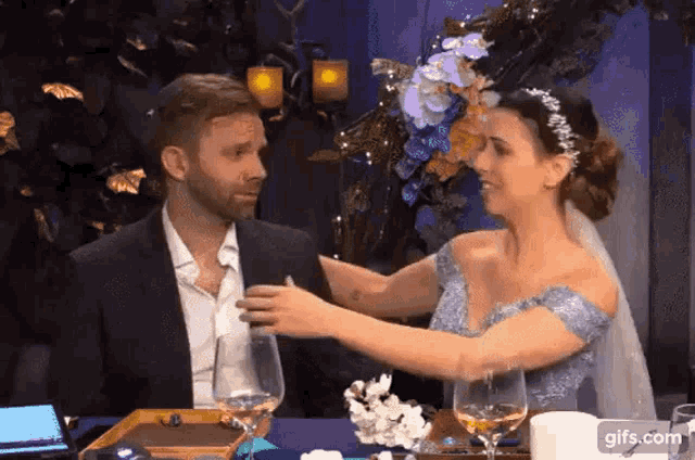 a bride and groom are sitting at a table with wine glasses .