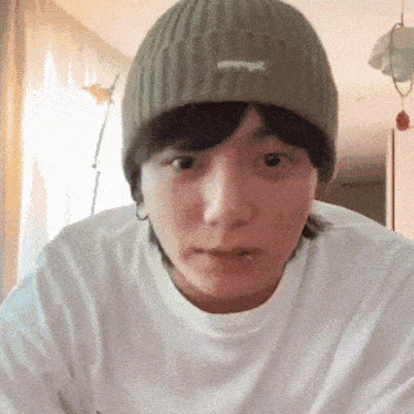 a person wearing a beanie and a white shirt looks at the camera
