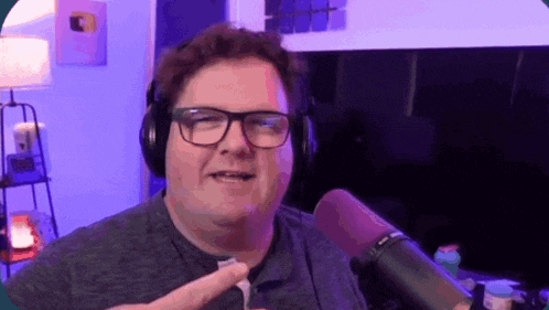 a man wearing headphones and glasses is standing in front of a microphone in a room .