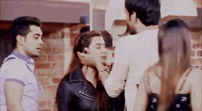 a man is putting his hand on a woman 's face while a group of people are standing around .