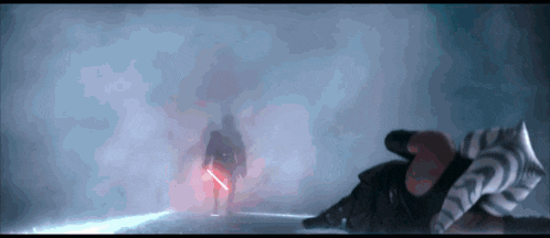 a man holding a red lightsaber is standing in the dark