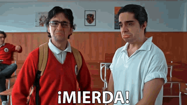 two men are standing in a classroom with the word mierda written on the screen