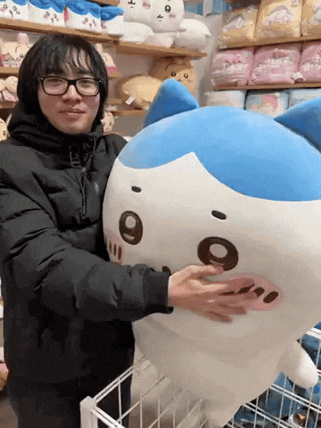 a man wearing glasses is holding a stuffed animal that looks like a cat .