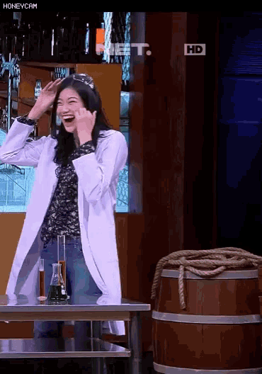 a woman in a lab coat is laughing in front of a sign that says hd on it