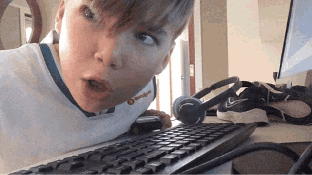 a boy wearing a shirt that says ' teamsport ' on it is laying on a computer keyboard