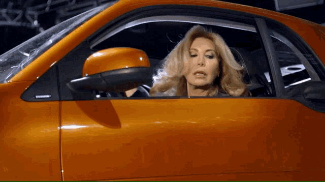 a woman is sitting in an orange car and looking out of the window
