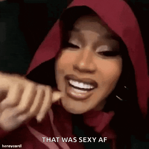 a woman in a red hoodie is smiling and holding a finger to her mouth .