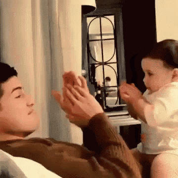 a man is holding a baby in his arms and the baby is clapping at the man 's hands .