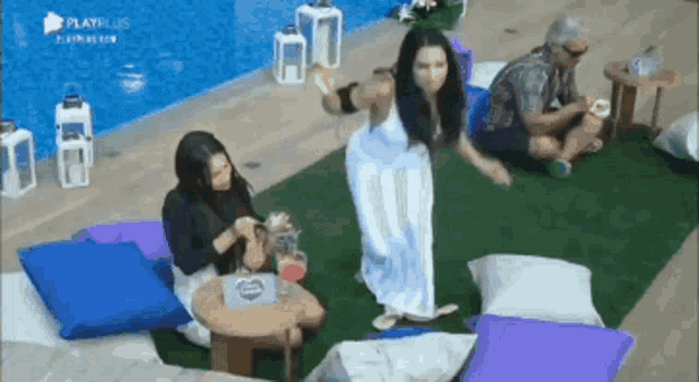 a woman in a white dress is dancing in front of a pool while a man sits on the ground .