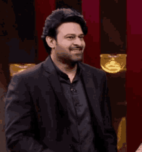 a man in a black suit and black shirt is smiling .