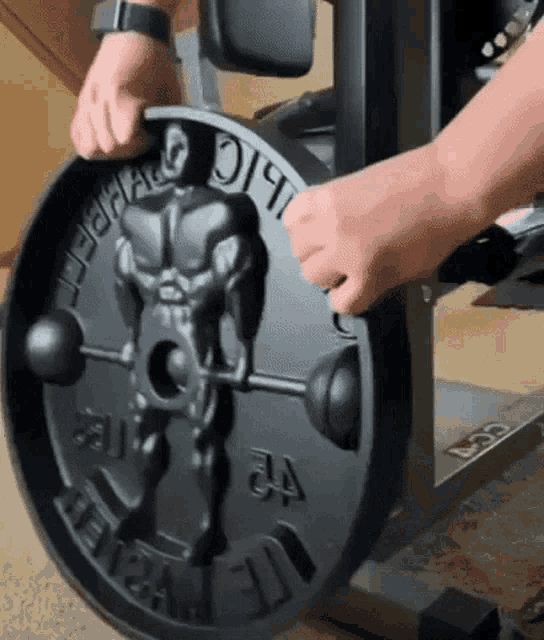 a person is holding a weight plate with a statue of a man lifting a barbell on it