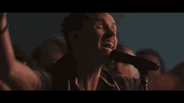 a man singing into a microphone with a crowd behind him