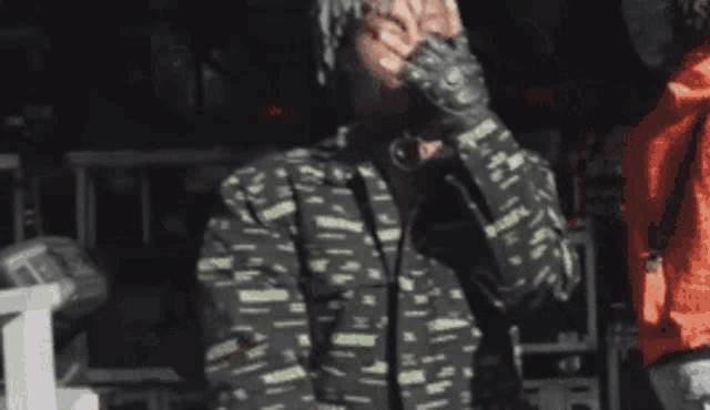 a man wearing a black and green jacket is covering his face with his hand .