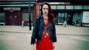 a woman in a leather jacket stands in front of a shorty 's saloon