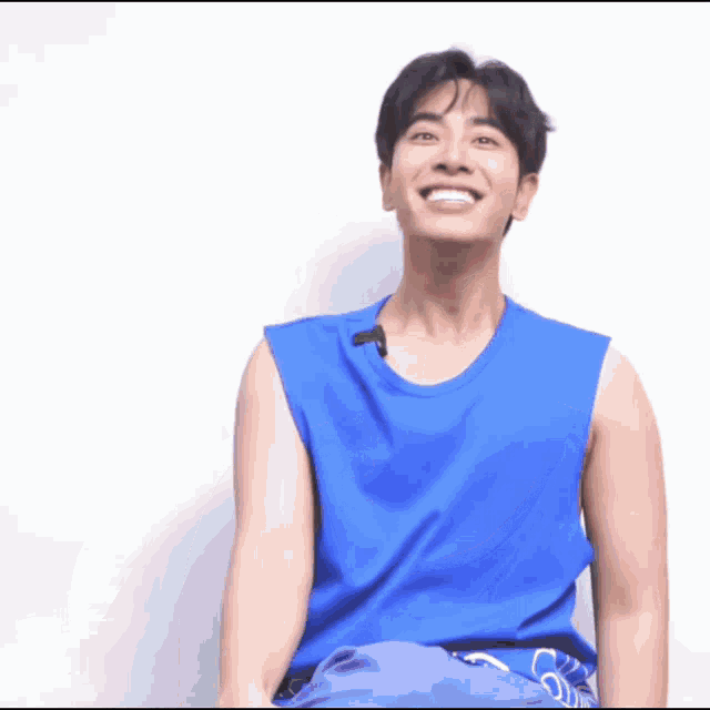 a young man wearing a blue tank top smiles for the camera