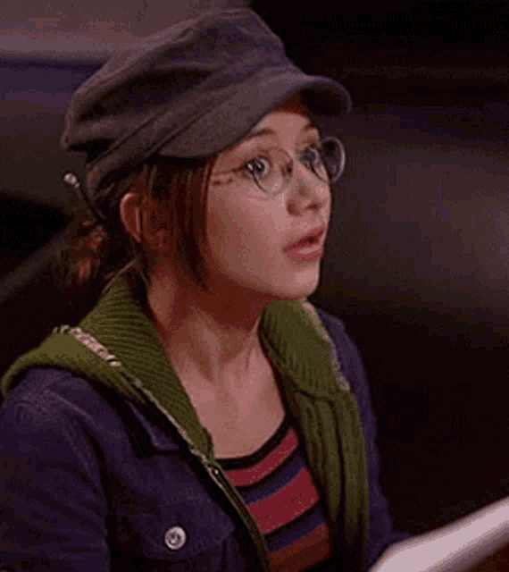 a young woman wearing glasses and a hat is sitting at a table .