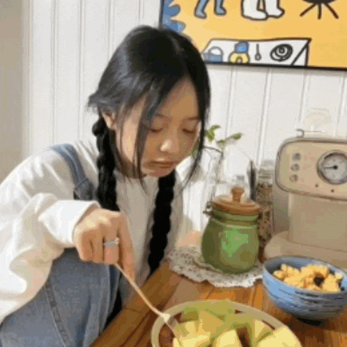 a young girl is sitting at a table eating food with a spoon .