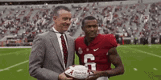 a man in a suit and tie is holding a football next to a football player in a red jersey with the number 6 .